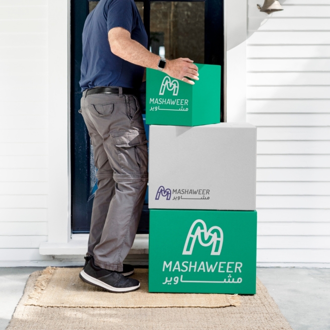 delivery man carriying delivery posts with mashaweer logo on it.